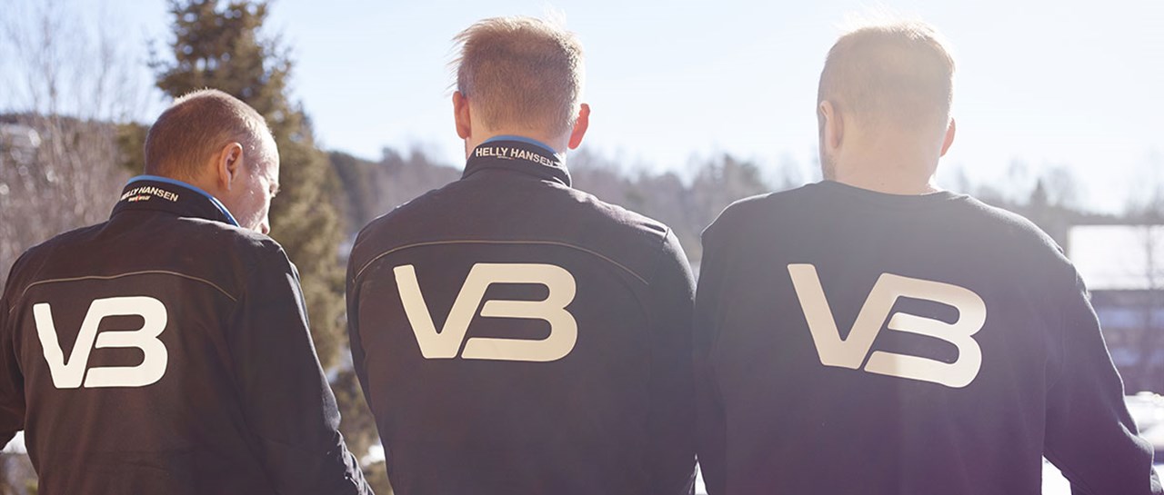 Tre VB Rørleggere som har på seg arbeidsklær med VB logo på ryggen